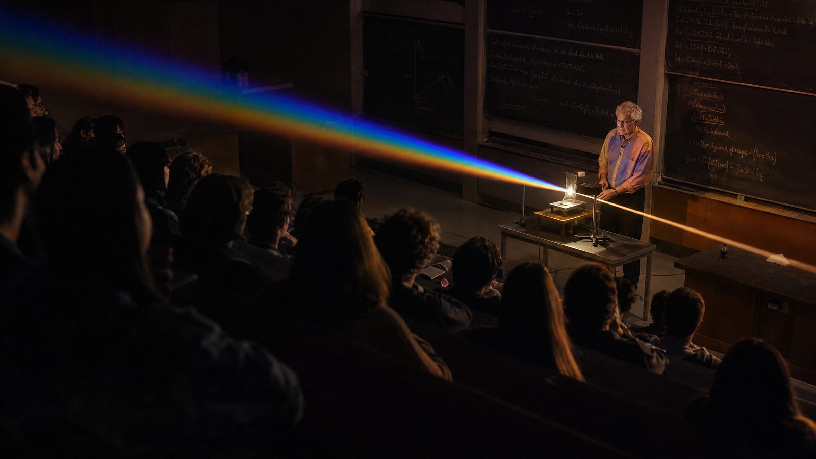 A professor demonstrating an optics experiment with light refracting through a prism in a university lecture hall